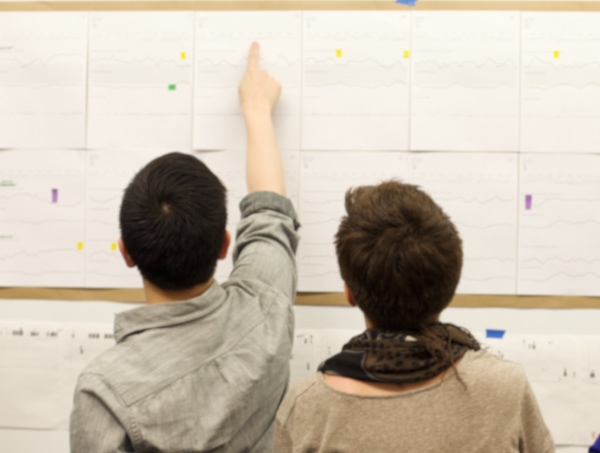 UX Product Designers pointing up at user data posted on a whiteboard