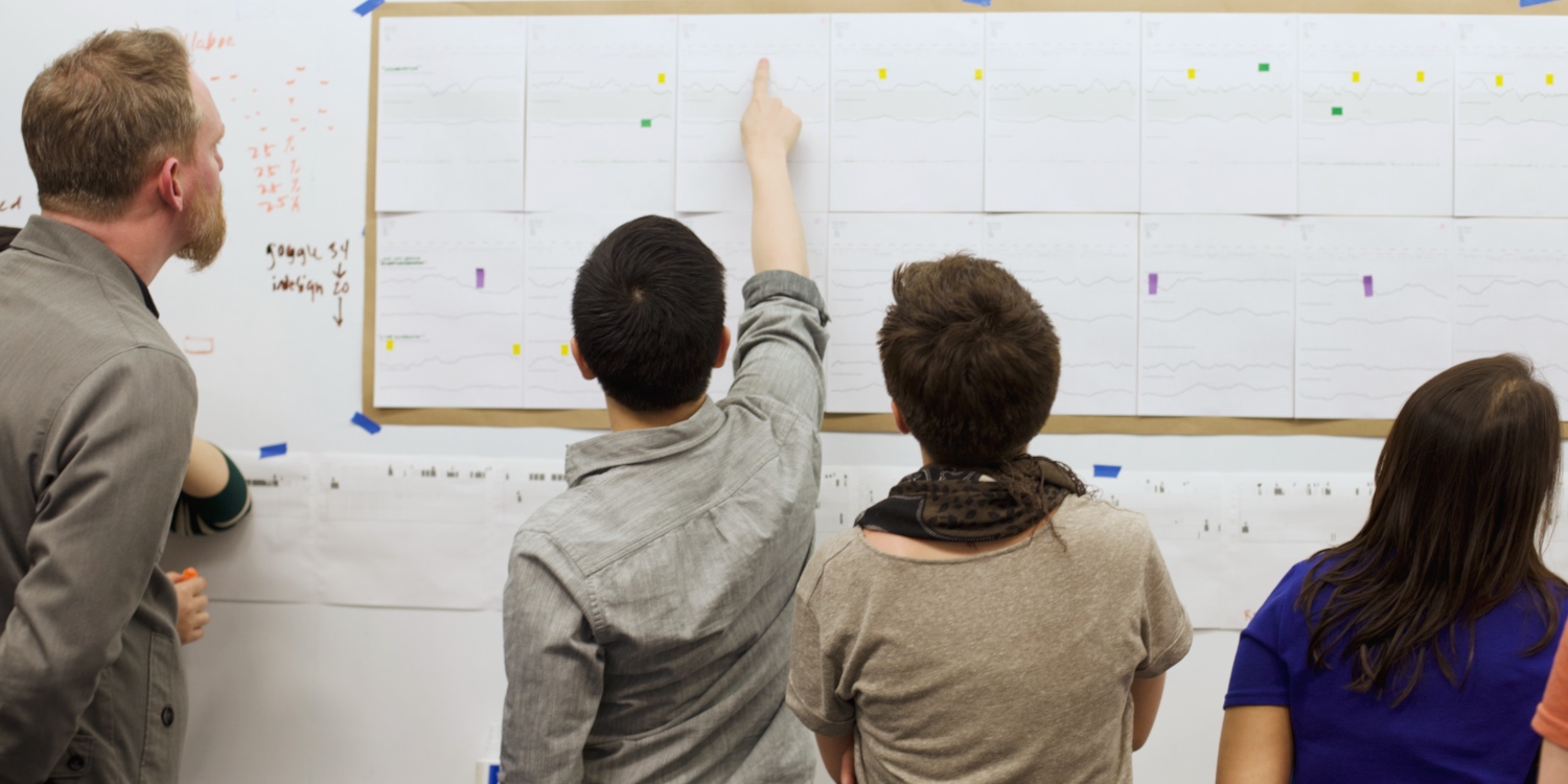 UX Product Designers pointing up at user data posted on a whiteboard