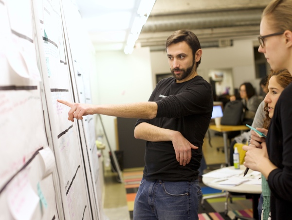 3 UX designers debating user research findings at a whiteboard in an office environment