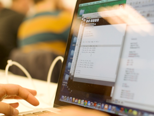 Hands at a keyboard with code on the screen and blurred people in the background